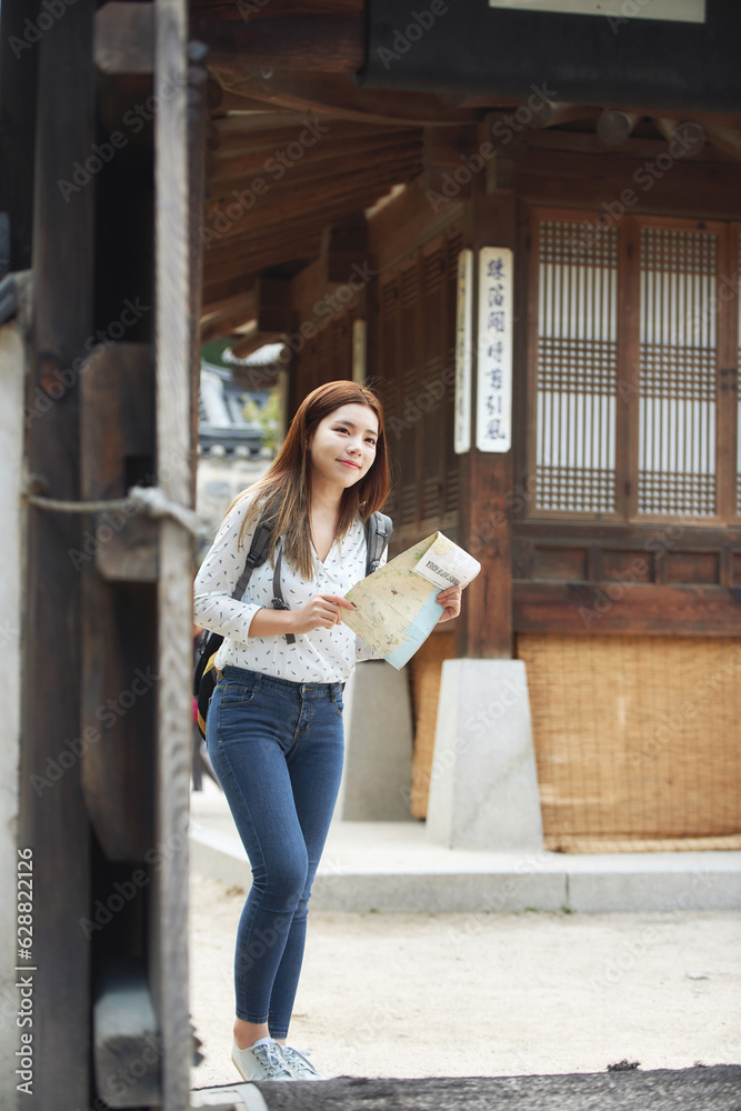 A young female college student who is looking for her way while looking at a map with a backpack in a traditional Korean village A young female college student who is looking for her way while looking at a map with a backpack in a traditional Korean village