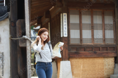 A young female college student who is looking for her way while looking at a map with a backpack in a traditional Korean village
