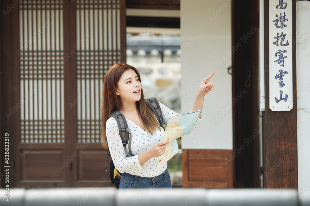 A young female college student who is looking for her way while looking at a map with a backpack in a traditional Korean village A young female college student who is looking for her way while looking at a map with a backpack in a traditional Korean village