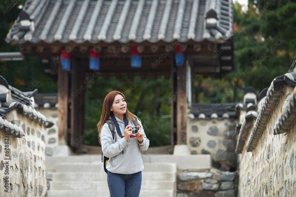 Fototapeta premium A young woman wearing a camera and taking pictures while traveling to tourist attractions with traditional Korean houses