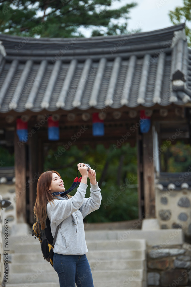 Fototapeta premium A young woman wearing a camera and taking pictures while traveling to tourist attractions with traditional Korean houses