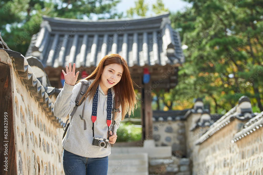 Fototapeta premium A young woman wearing a camera and taking pictures while traveling to tourist attractions with traditional Korean houses