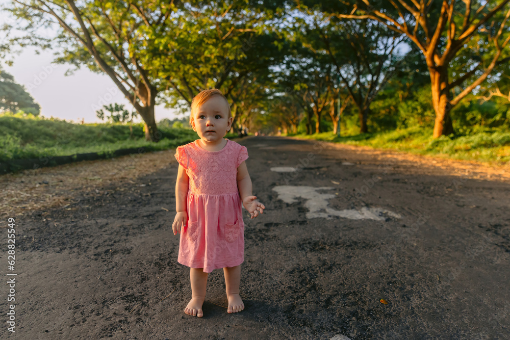 Beautiful infant girl in outdoor with sunset tones. Cute baby in pink dress in park. Beautiful infant girl in outdoor with sunset tones. Cute baby in pink dress in park.