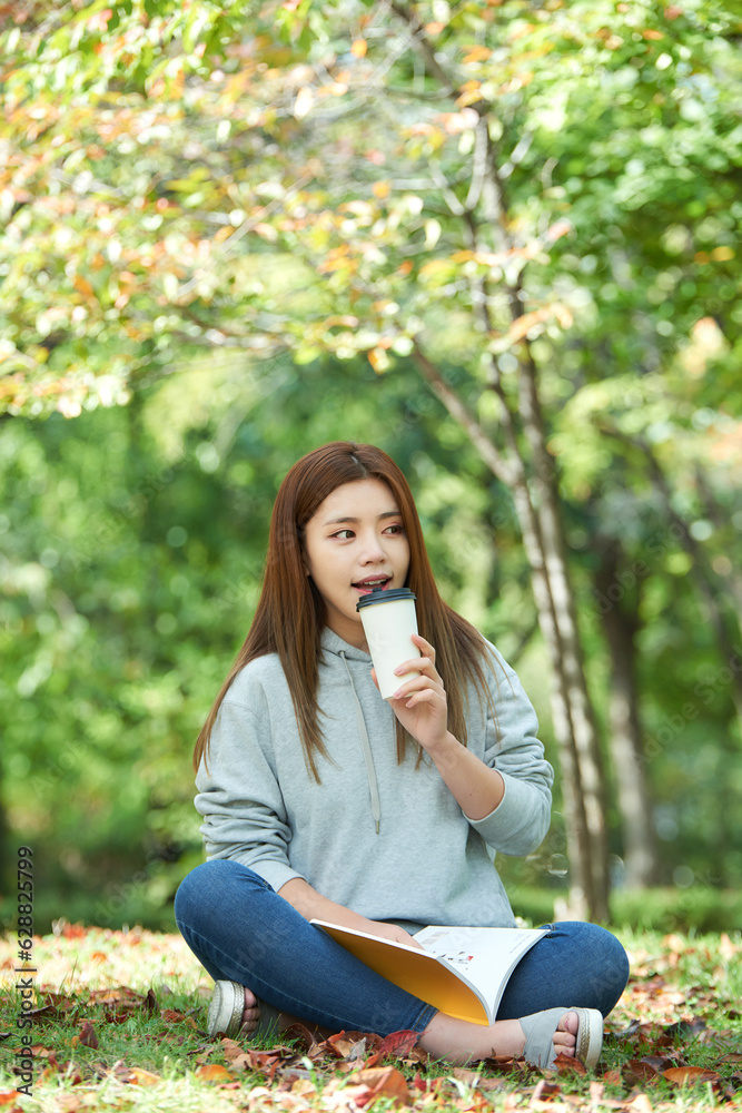 a young woman sitting in a forest park, drinking coffee and reading a young woman sitting in a forest park, drinking coffee and reading