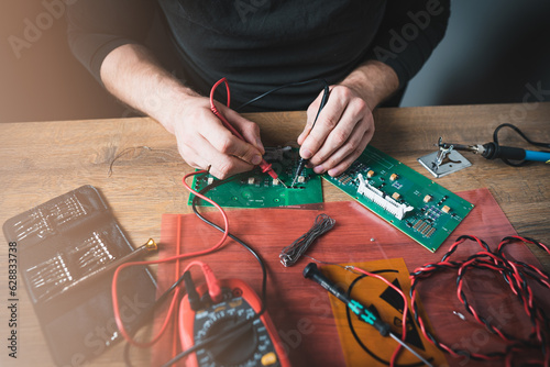 A man is checking the circuit of an electronic board with a multimeter. Fixing broken electonics.