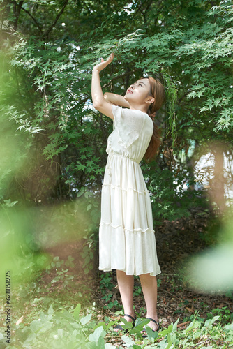 In summer daytime  a beautiful Asian woman wearing a dress in a forested park is doing various movements.