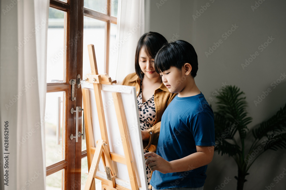 Asian Woman assisting young boy in painting on canvas. Happy woman looking at her painting .. Asian Woman assisting young boy in painting on canvas. Happy woman looking at her painting ..
