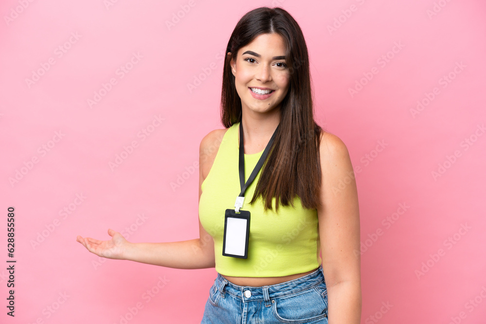 Young Brazilian woman with ID card isolated on pink background extending hands to the side for inviting to come Young Brazilian woman with ID card isolated on pink background extending hands to the side for inviting to come
