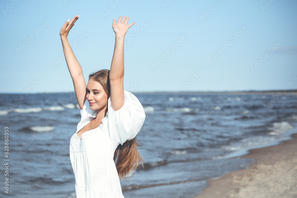 Happy smiling beautiful woman on the ocean beach standing in a white summer dress, raising hands Happy smiling beautiful woman on the ocean beach standing in a white summer dress, raising hands