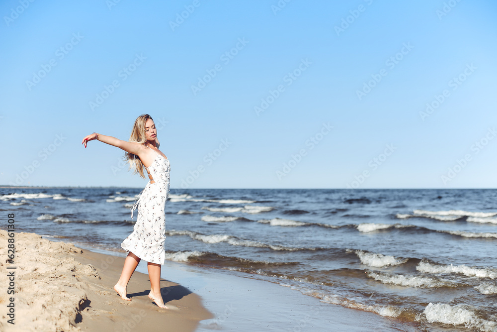 Happy blonde beautiful woman on the ocean beach standing in a white summer dress, open arms Happy blonde beautiful woman on the ocean beach standing in a white summer dress, open arms
