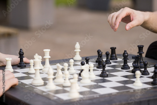 Closeup of a man's at a table and plays chess. The teenager picked up the chess piece and makes his move. Outdoors activities