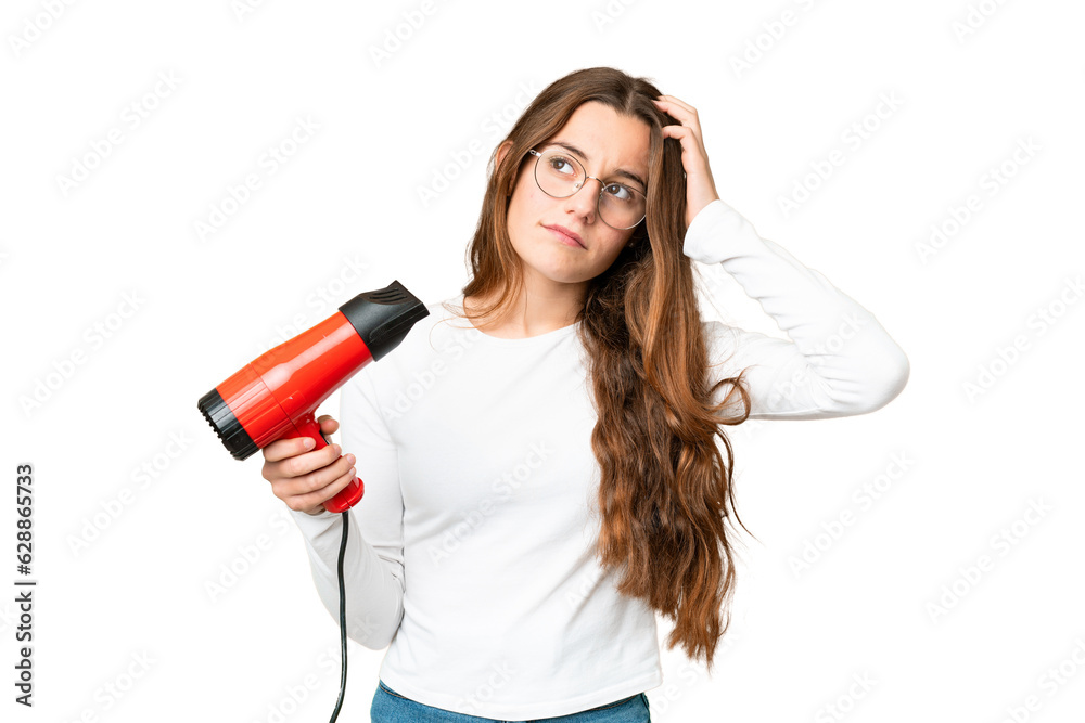Teenager girl holding a hairdryer over isolated chroma key background having doubts and with confuse face expression Teenager girl holding a hairdryer over isolated chroma key background having doubts and with confuse face expression