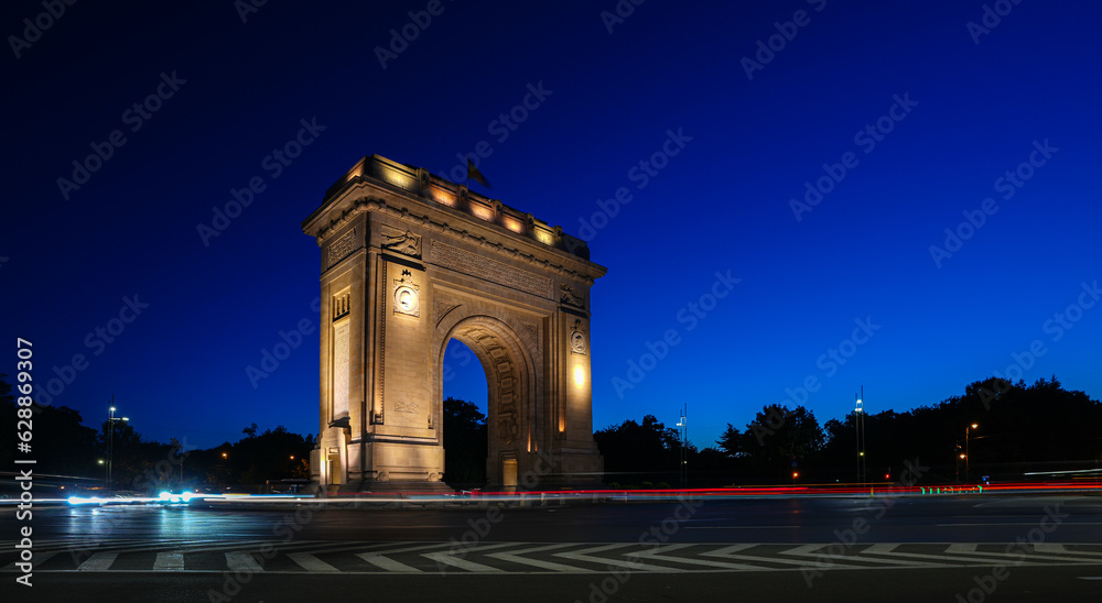 Bucharest long exposure night photo. Early morning with clean blue sky at Arch of Triumph historical landmark from Romania. Traffic lights in foreground.