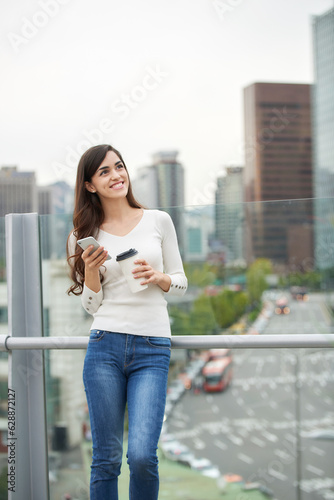 A young woman is resting on a land bridge with coffee and a smartphone in the background of a busy street during the day. © PHOTOGRAPHER JH