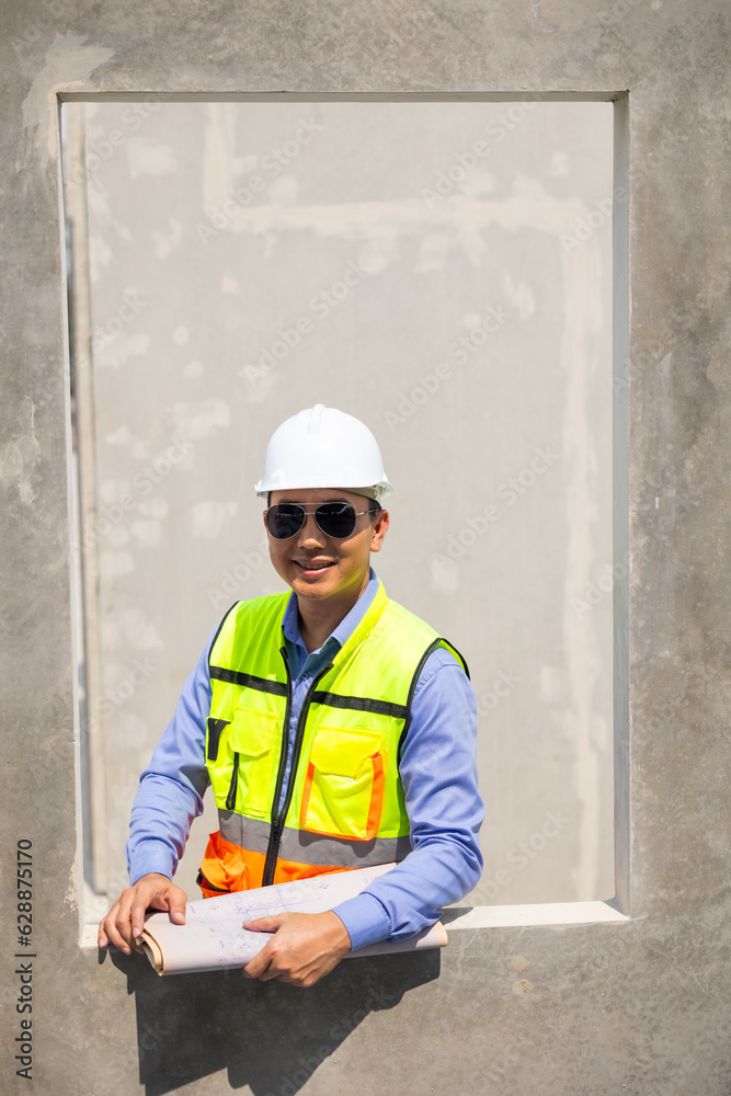 Asian male portrait. architect Engineering man in safety hardhat looking at blueprint at factory industrial facilities. Heavy Industry Manufacturing Factory. Prefabricated concrete walls Asian male portrait. architect Engineering man in safety hardhat looking at blueprint at factory industrial facilities. Heavy Industry Manufacturing Factory. Prefabricated concrete walls