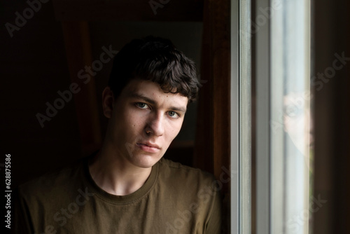 Dramatic portrait of a young man in a house near a window, the guy is sad, he needs real friendships to get out of depression, the guy has a headache