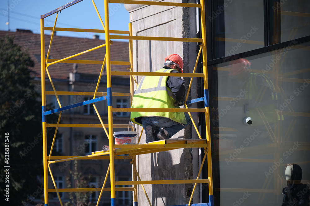 A worker in a helmet and vest works with the facade of the building
