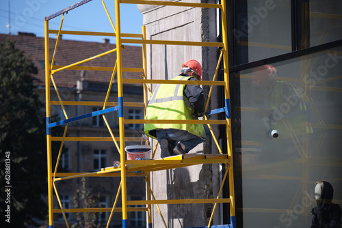 A worker in a helmet and vest works with the facade of the building