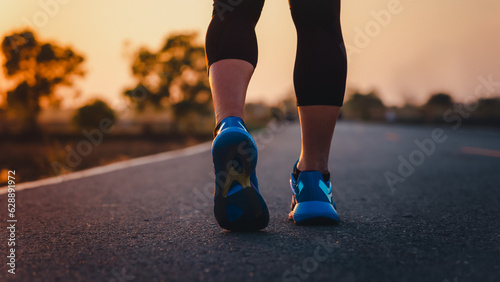 Rear view of a man's feet before running. Adult man doing exercise running and walking on country road in the morning with sunrise background. Concept of health and lifestyle.