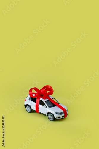 White model car with bow on a yellow background. Car as gift, surprise