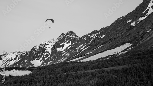 Grayscale of a man paragliding, his parachute billowing in the wind