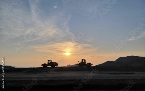 Two industrial vehicles parked on top of a hill with a beautiful sunset in the background