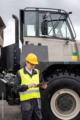 Engineer with tablet computer stands next to mining truck
