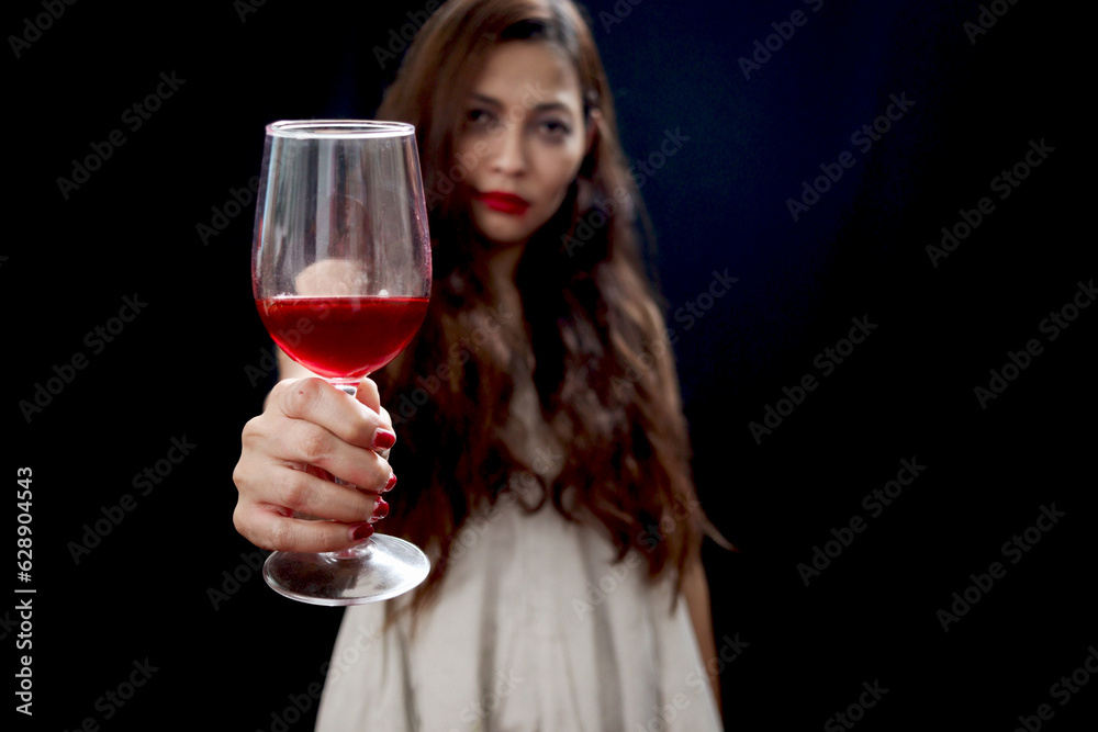 Red wine glass in hand of beautiful black long hair woman white ghost spooky costume in dark background, scary dead corpse female holding wine glass to celebrate Halloween party night. Red wine glass in hand of beautiful black long hair woman white ghost spooky costume in dark background, scary dead corpse female holding wine glass to celebrate Halloween party night.