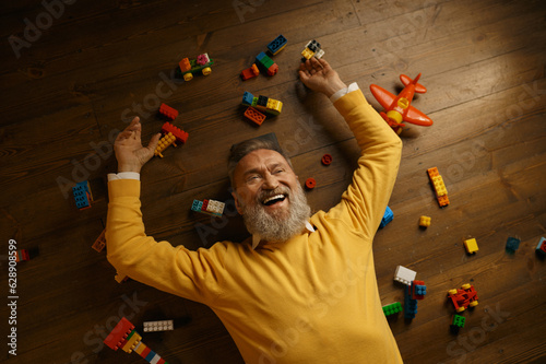 Happy senior man lying on floor with scattered toy building blocks