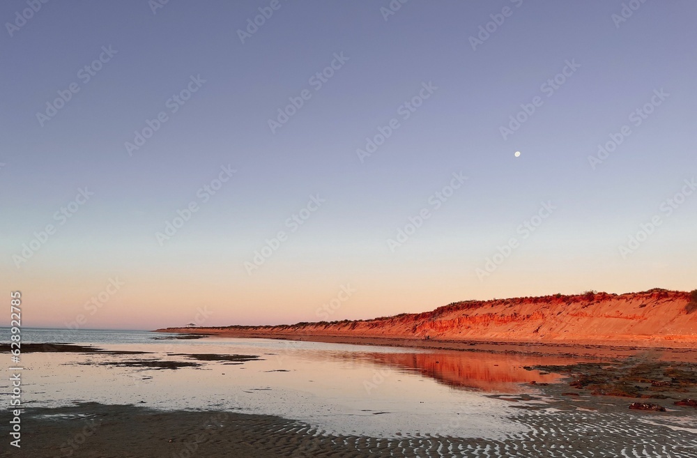 Stunning landscape with a tranquil beach and vibrant red cliffs reflected in the ocean at sunset