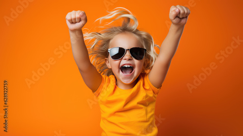 Small child shouts loudly while raising hands up in victory against isolated bright orange background.