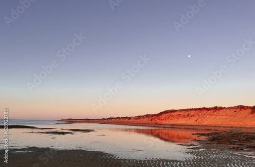 Stunning landscape with a tranquil beach and vibrant red cliffs reflected in the ocean at sunset