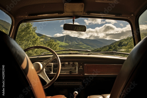 View from the back seat of a old car. The view through the windshield is of a mountainous landscape with green trees and blue sky