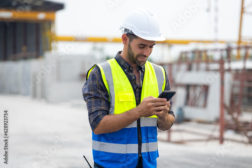 building and construction worker using mobile phone, Hiapanic latin male wearing safety hard hat helmet standing with arms crossed at construction site and looking at camera