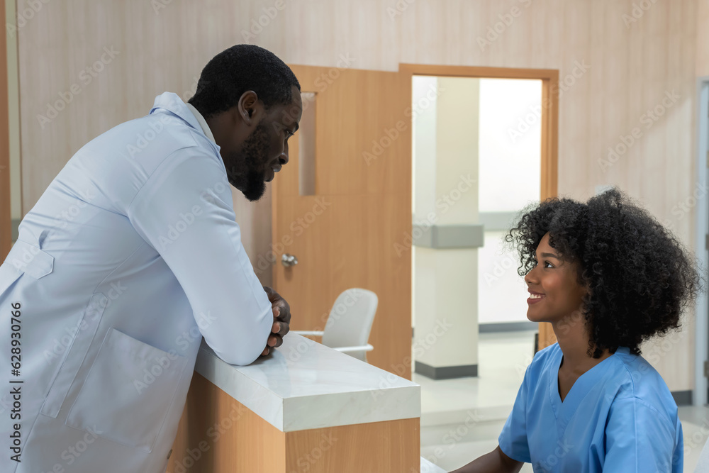 Black doctor in white gown talking with black nurse at registration desk in hospital 