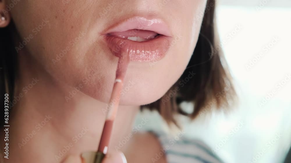 Young beautiful woman applying gloss to her lips doing make-up. Young beautiful woman applying gloss to her lips doing make-up.