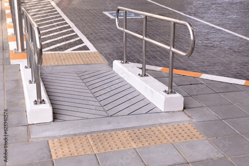 wheelchair concrete ramp way with yellow braille block tiles and stainless steel handrail, ramp for support disabled persons in parking area for handicapped
