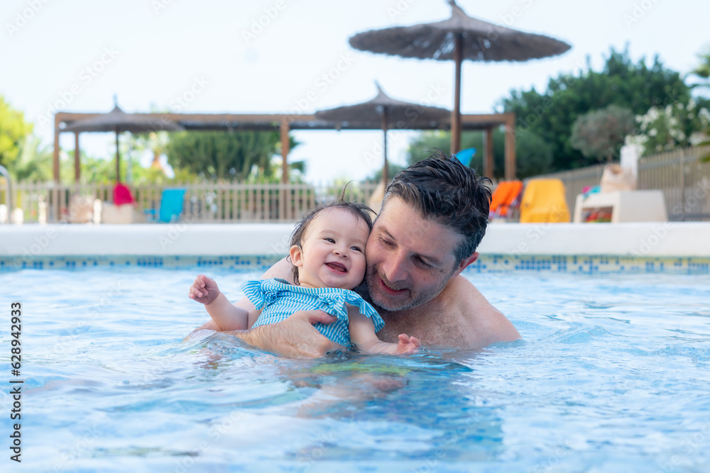 lifestyle portrait of father and little daughter enjoying summer - man holding her sweet baby girl excited and cheerful playing together at resort swimming pool in parenting concept