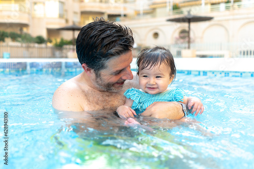 lifestyle portrait of father and little daughter enjoying summer - man holding her sweet baby girl excited and cheerful playing together at resort swimming pool in parenting concept © TheVisualsYouNeed