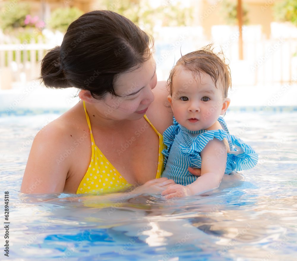 happy and beautiful Asian woman holding her little baby girl playful - Korean mother and adorable daughter playing on water at resort swimming pool in Summer happy and beautiful Asian woman holding her little baby girl playful - Korean mother and adorable daughter playing on water at resort swimming pool in Summer