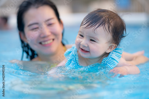 happy and beautiful Asian woman holding her little baby girl playful - Korean mother and adorable daughter playing on water at resort swimming pool in Summer