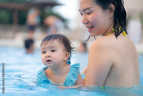 happy and beautiful Asian woman holding her little baby girl playful - Korean mother and adorable daughter playing on water at resort swimming pool in Summer