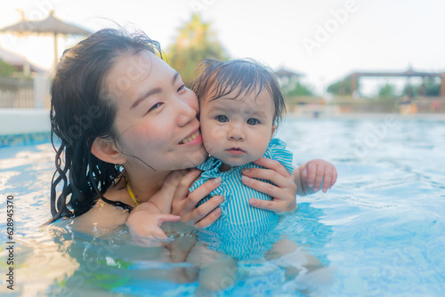 happy and beautiful Asian woman holding her little baby girl playful - Korean mother and adorable daughter playing on water at resort swimming pool in Summer