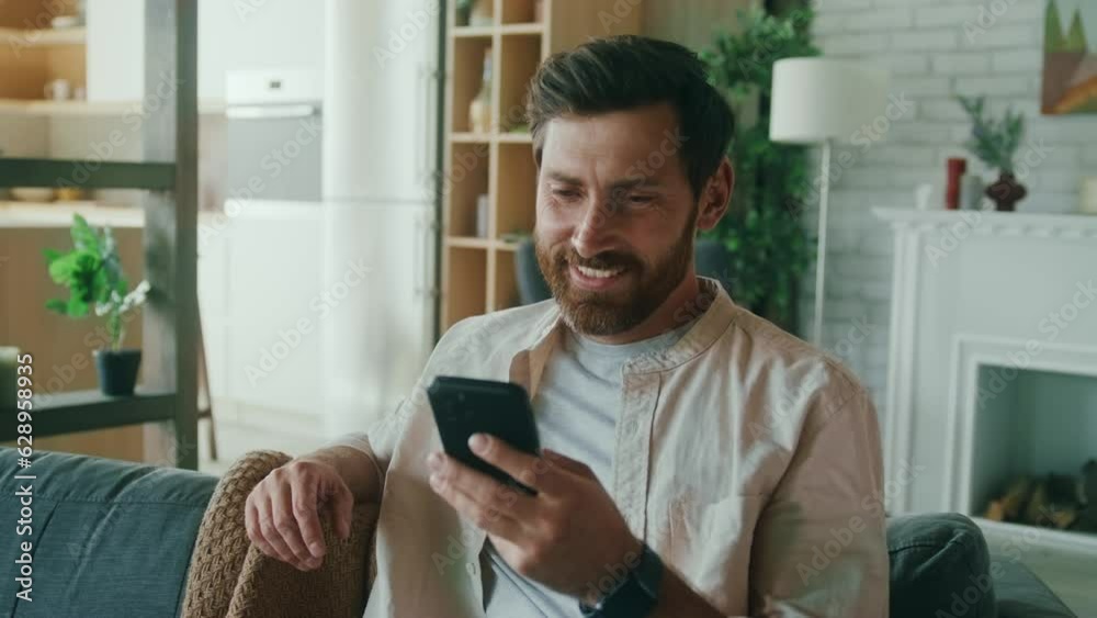 Caucasian man happily typing on the phone and smiling at home Caucasian man happily typing on the phone and smiling at home