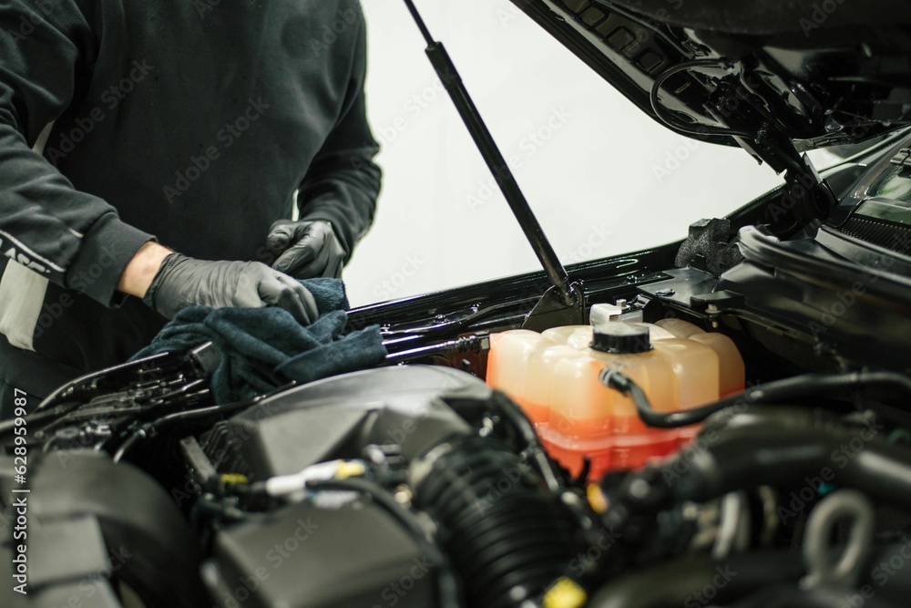 Mechanic standing in front of a car, its hood open to reveal the engine compartment Mechanic standing in front of a car, its hood open to reveal the engine compartment