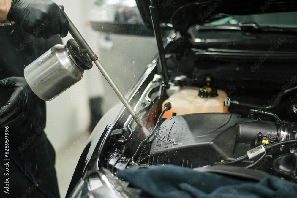 Worker wearing protective gloves is spraying a car engine with a can of cleaning solution