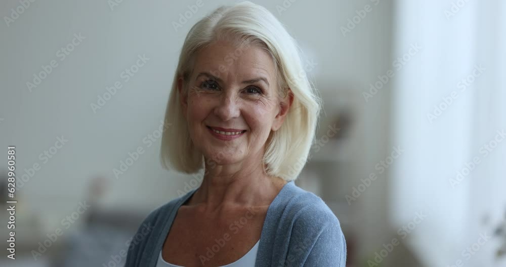 Pretty blonde senior elderly woman turning look at camera, getting positive, happy, smiling, laughing, posing indoors. Cheerful old lady in casual indoor portrait
