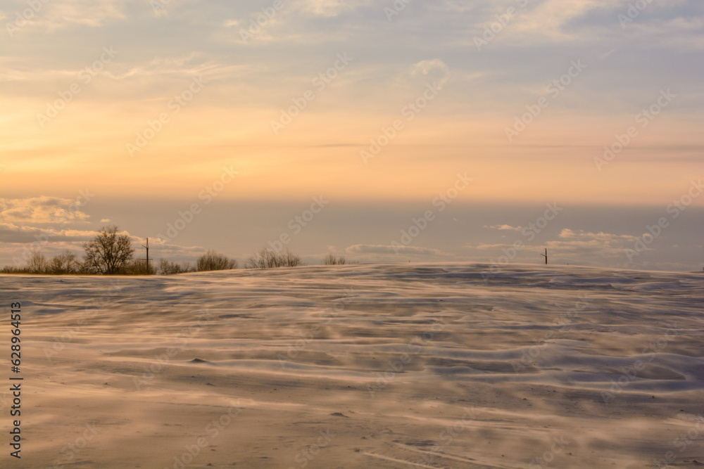 sandy hill covered with snow, against a blue sky with long white clouds, during a bright sunset, during the golden hour sandy hill covered with snow, against a blue sky with long white clouds, during a bright sunset, during the golden hour