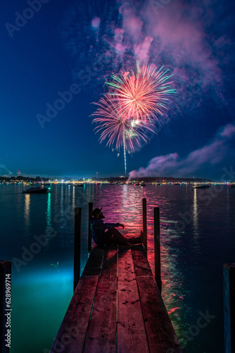 Man sitting on wooden dock watching fireworks over the lake