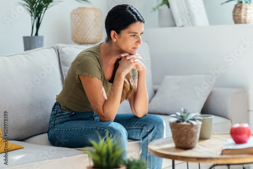 Foto Worried sad woman thinking while sitting on couch in the living room at home